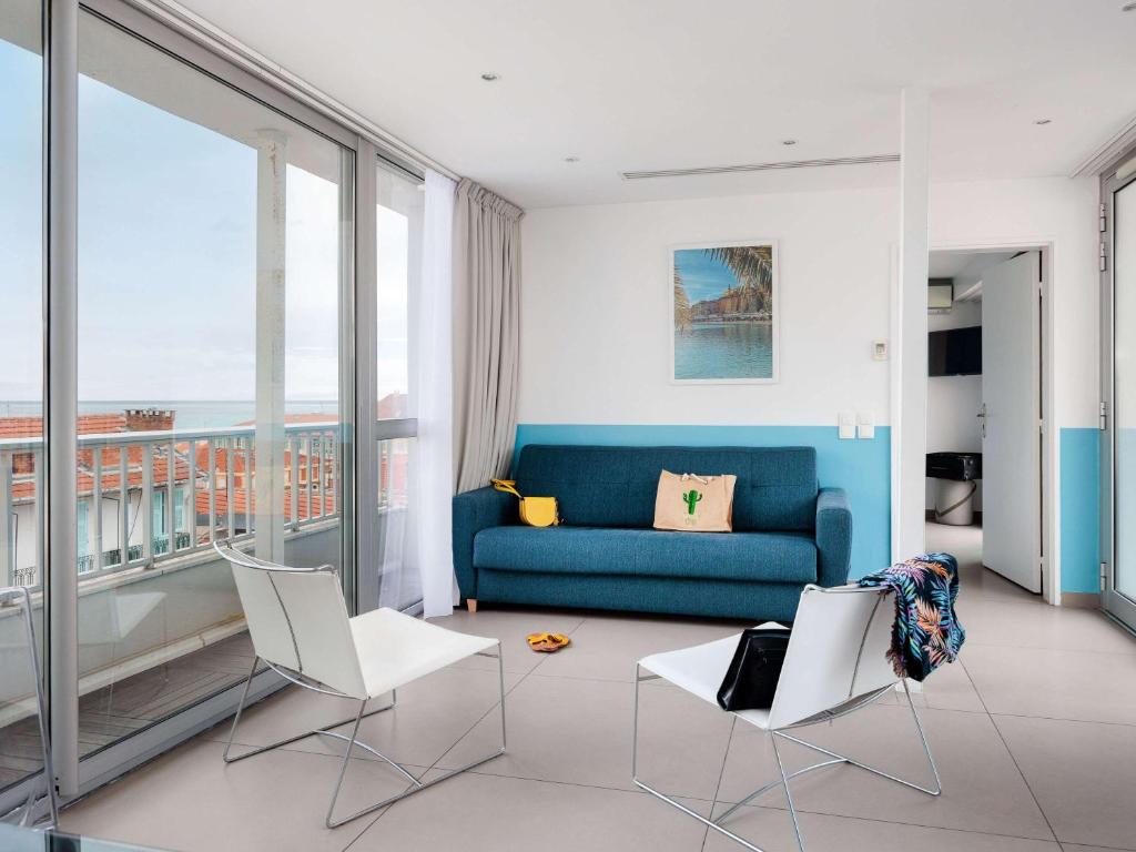 a living room with a blue couch and white chairs at Ibis Styles Menton Centre in Menton