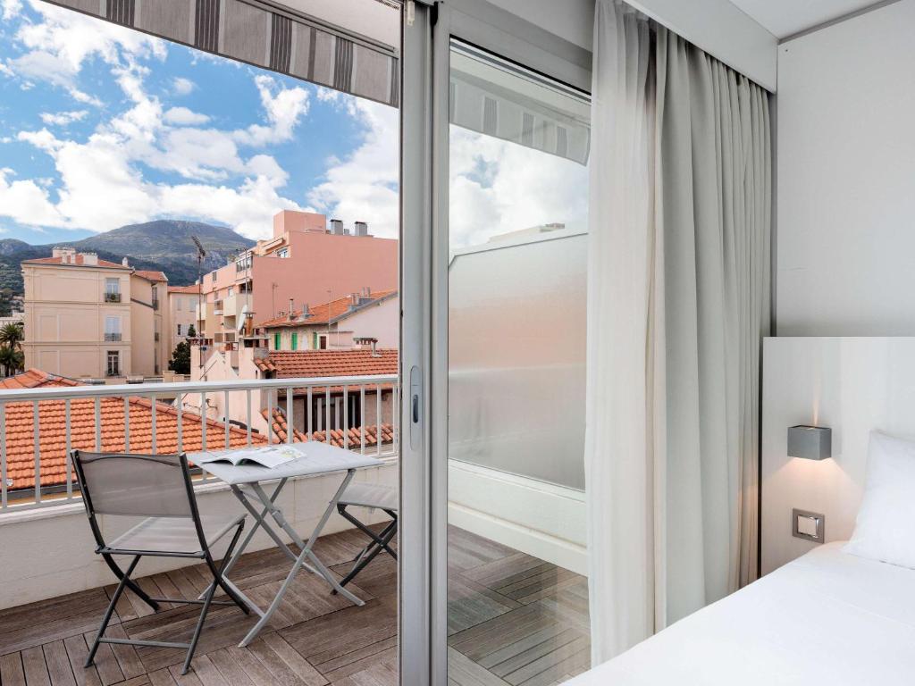 a bedroom with a bed and a table and a balcony at Ibis Styles Menton Centre in Menton