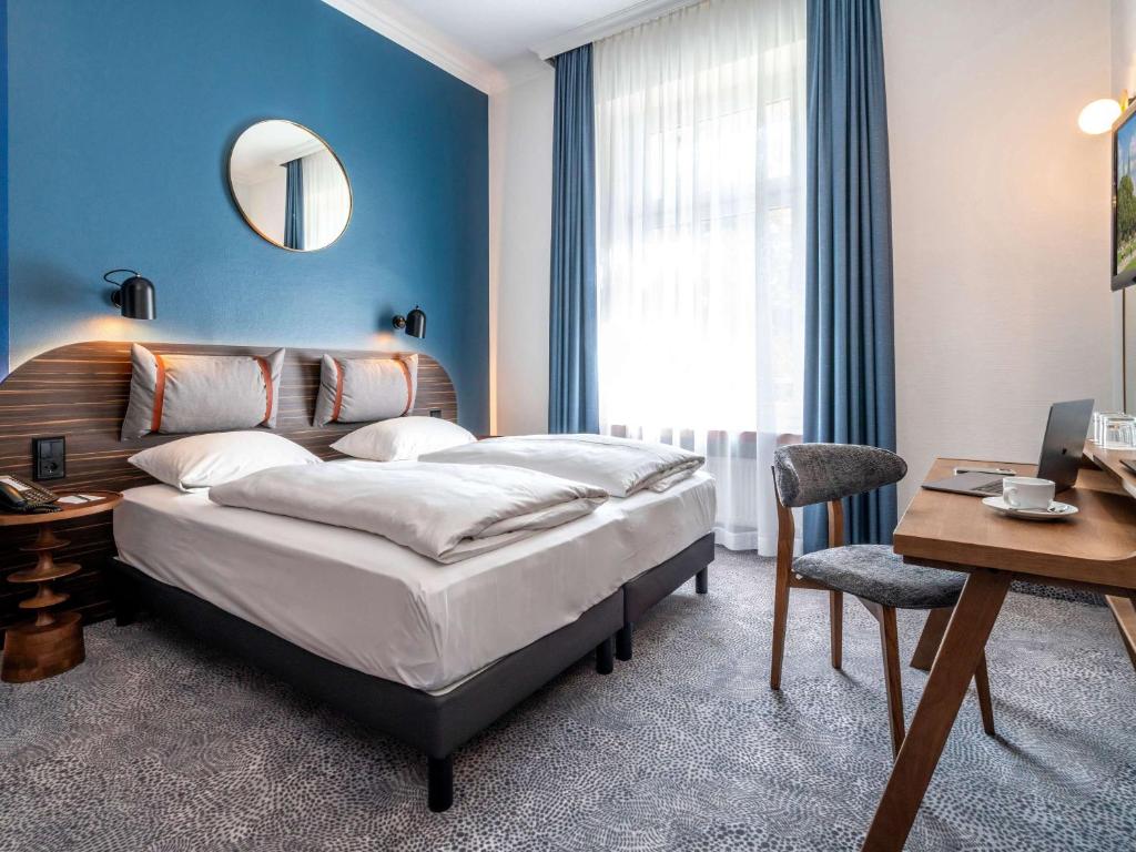 a hotel room with a bed and a desk and a mirror at Mercure Hotel Luebeck City Center in Lübeck