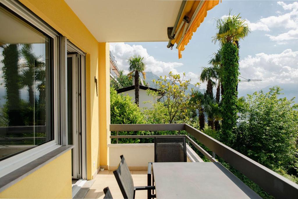 einen Balkon mit einem Tisch, einem Fenster und Palmen in der Unterkunft Residenza la Promenada App 4242 in Orselina