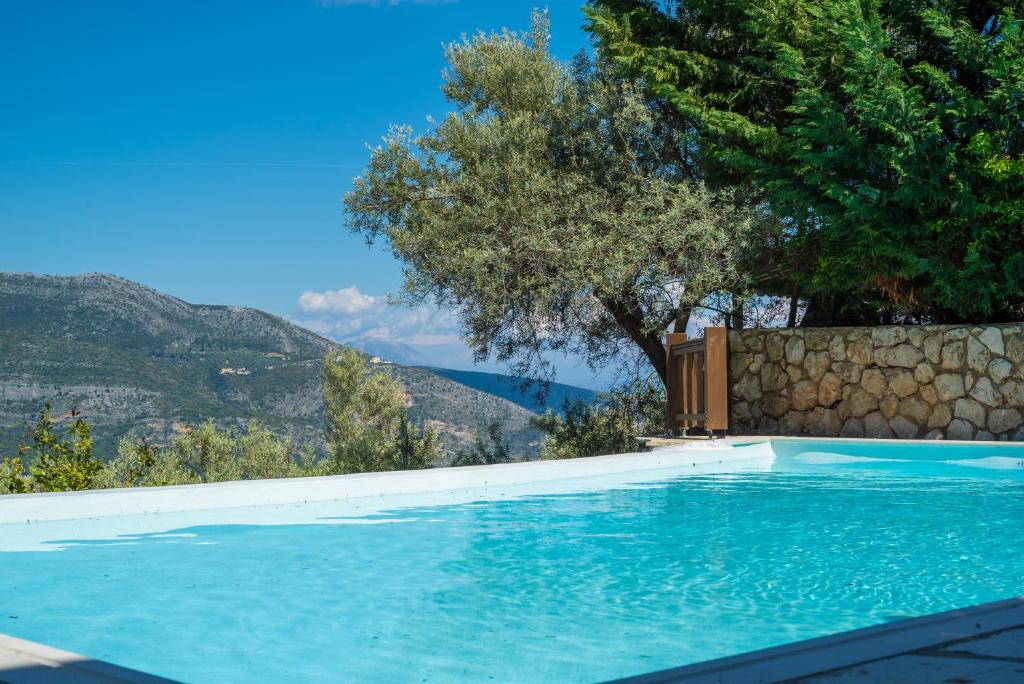 a swimming pool with a tree and mountains in the background at Arriva Villas in Sivota