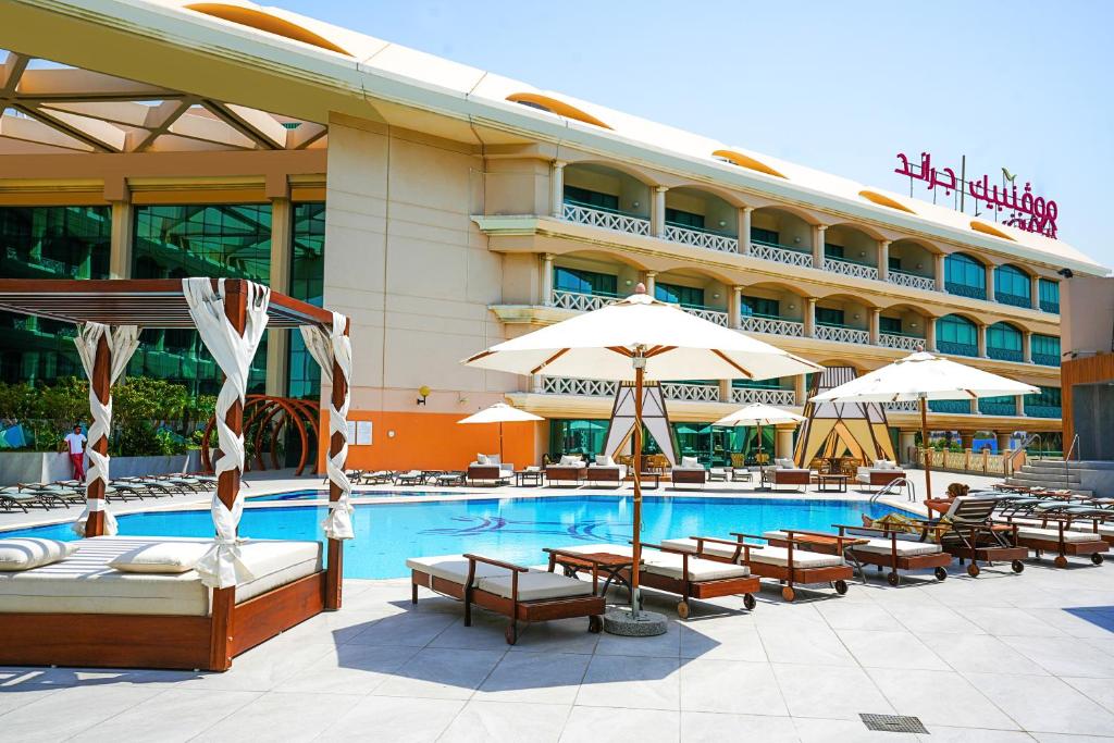 a hotel with a swimming pool with chairs and umbrellas at Mövenpick Grand Al Bustan in Dubai