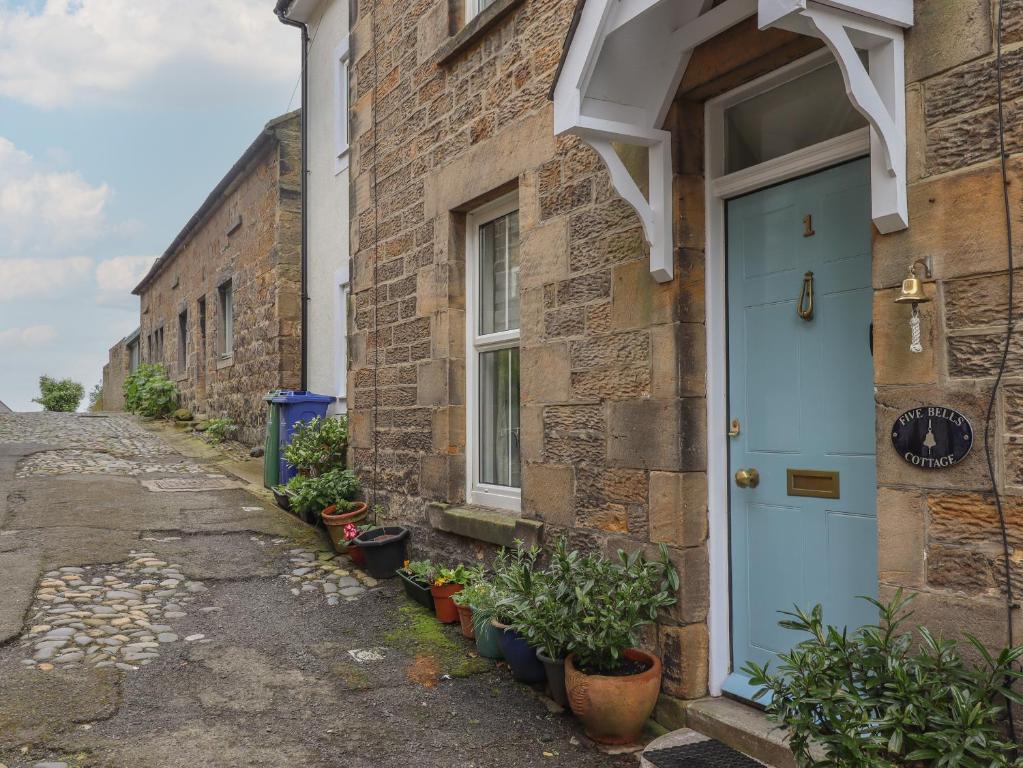 a brick building with a blue door and potted plants at Five Bells Cottage in Alnmouth