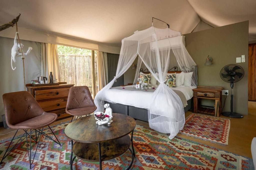 a bedroom with a canopy bed and two chairs at Umkumbe Bush Lodge - Luxury Tented Camp in Skukuza