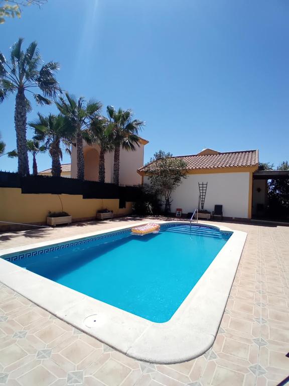 a swimming pool in front of a house with palm trees at Casa el Olivo in Mazarrón