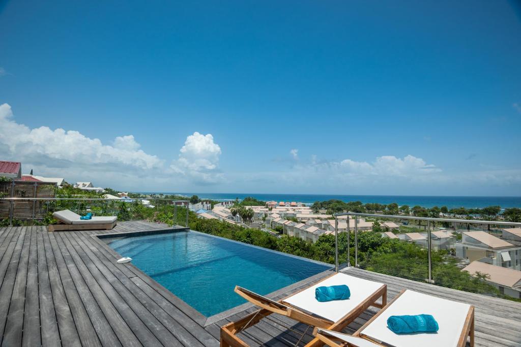 una piscina en una terraza con sillas y el océano en Résidence Les Raisins Clairs - Villas standing 4 étoiles , vue sur mer panoramique & piscine à débordement, en Saint-François