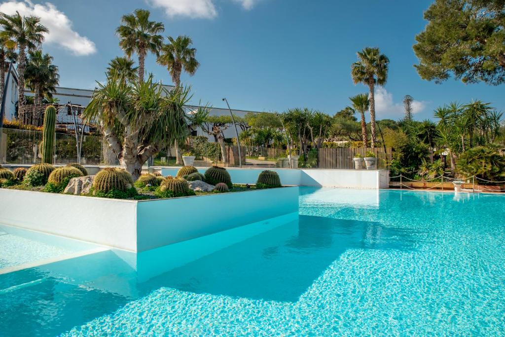 a swimming pool with blue water and palm trees at Villa Favorita Hotel & Events in Marsala