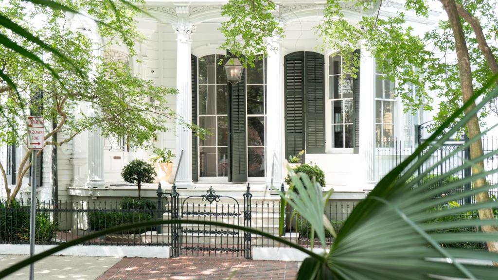 a white house with a black gate and trees at Roomza New Orleans at Melrose Mansion in New Orleans