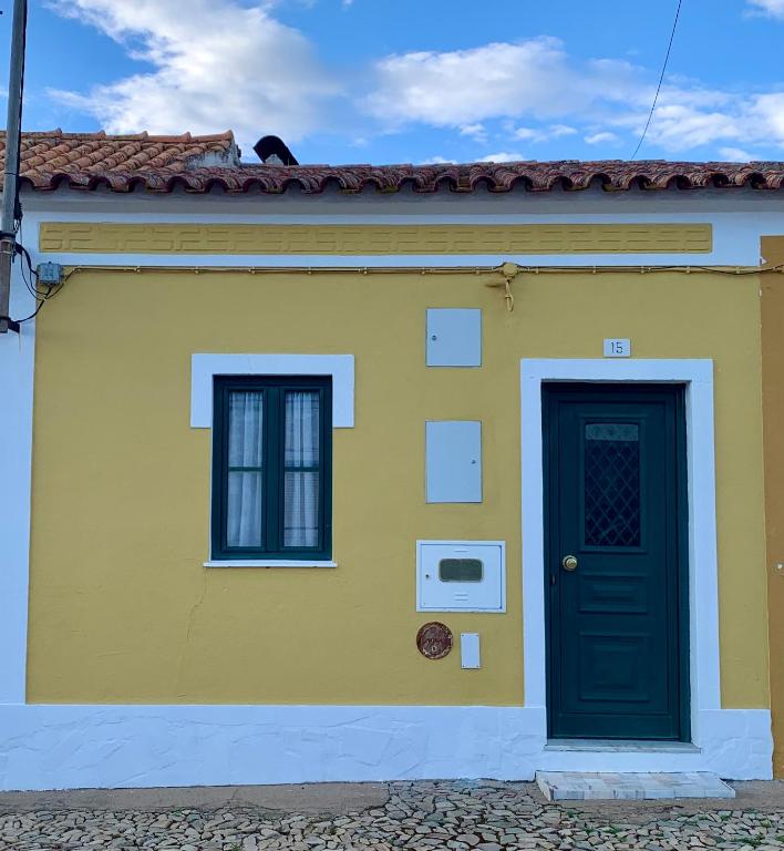 a yellow house with a black door and two windows at Casa da Tia Julia in Avis