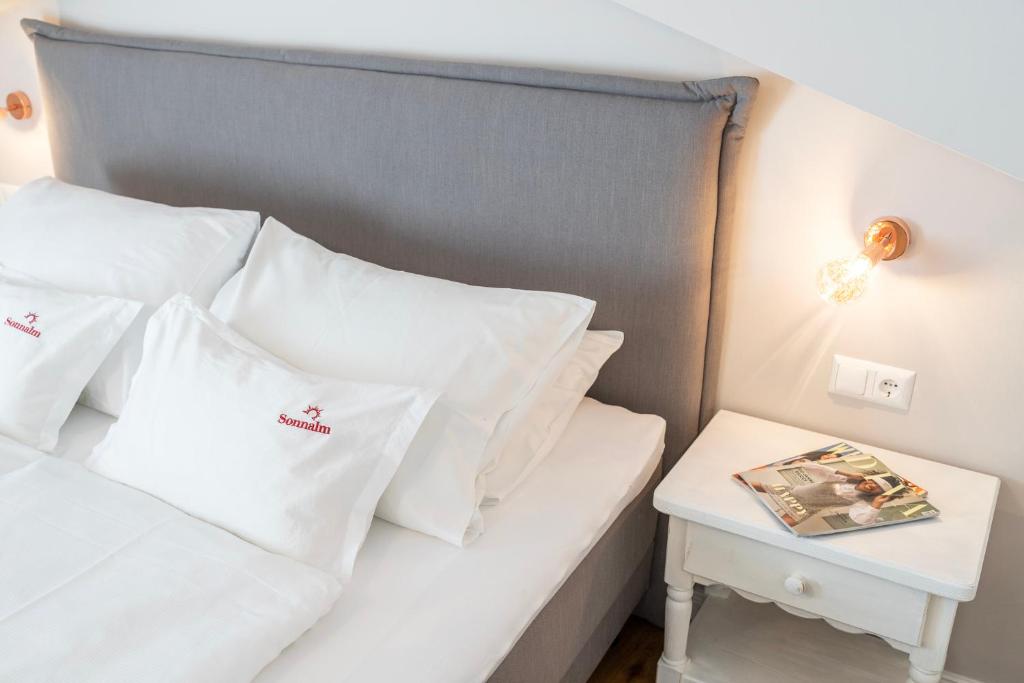 Hotel Sonnalm في باد كلينكيرشهايم: سرير بمخدات بيضاء وطاولة جانبية