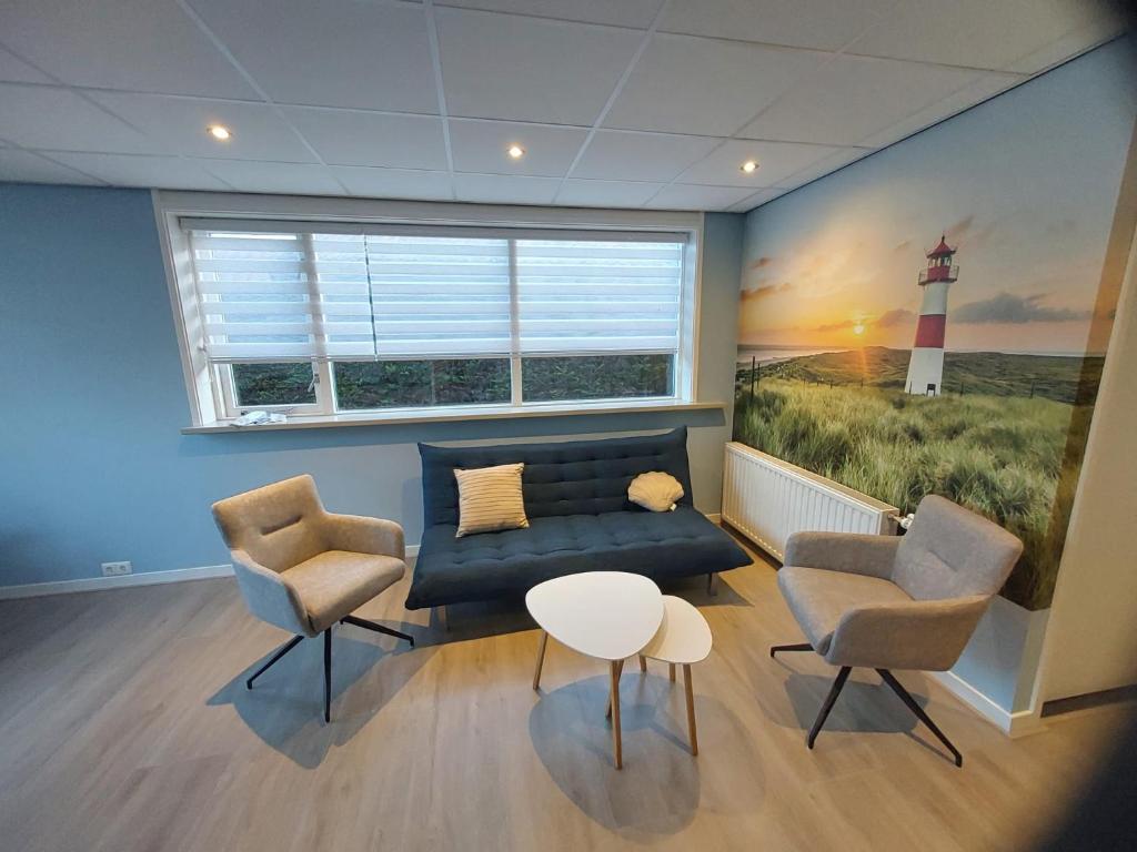 een woonkamer met een bank en twee stoelen en een schilderij van een vuurtoren bij 't Vakansie'uus in Serooskerke