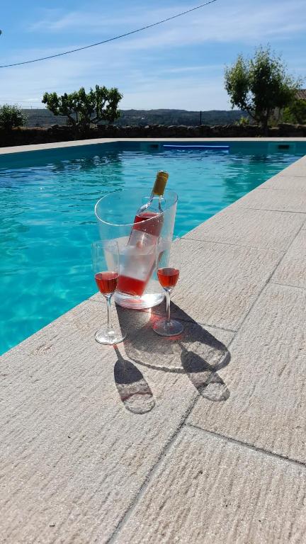 two glasses of wine sitting on a table next to a pool at Casinha CB in Casteição