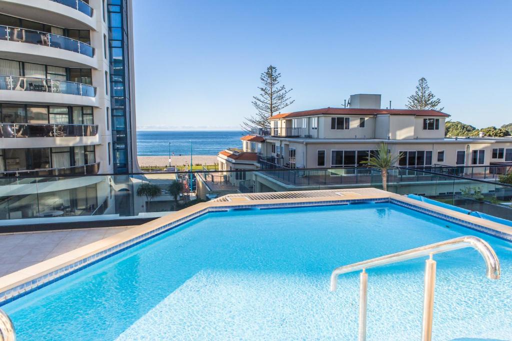 a swimming pool with a view of a building and the ocean at Eleven_at_Mauao in Mount Maunganui