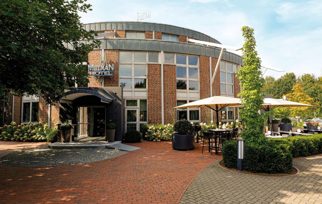a building with tables and umbrellas in front of it at Median Hotel Hannover Lehrte in Lehrte