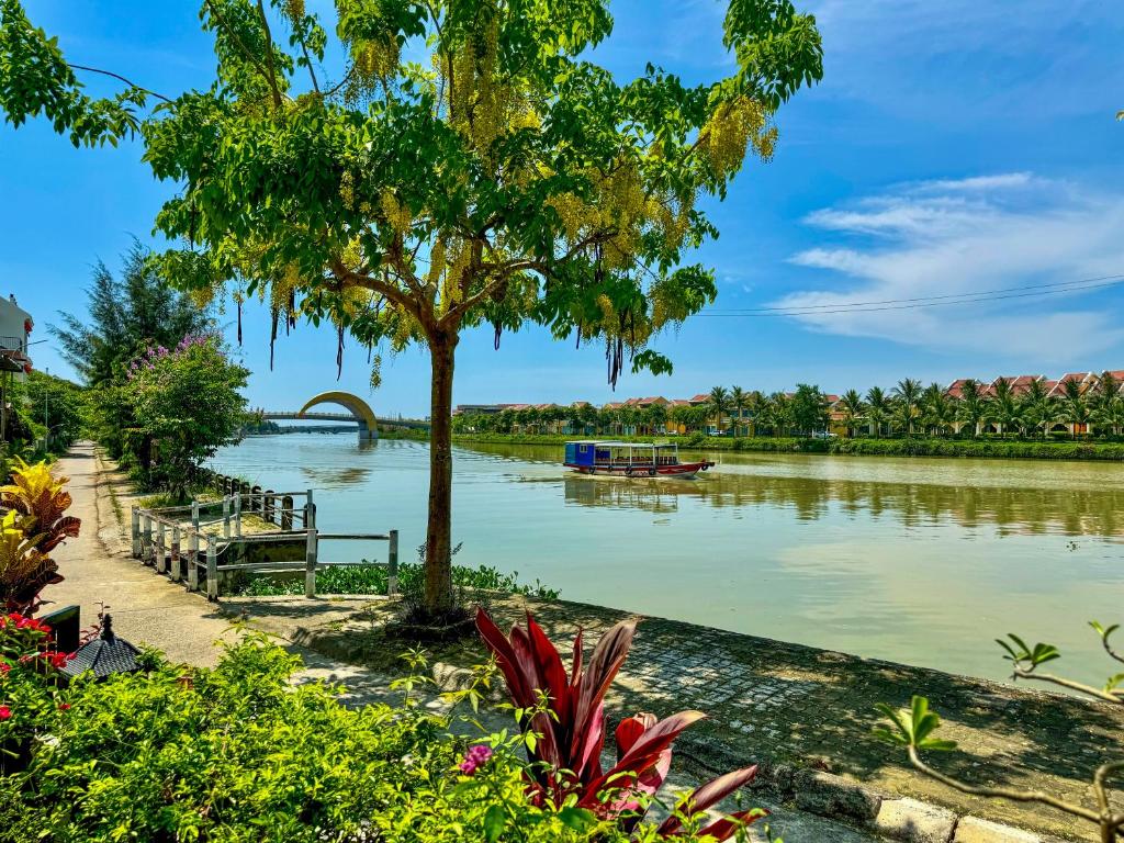 a river with a tree and a boat in the water at Riverside White House Hotel in Hoi An