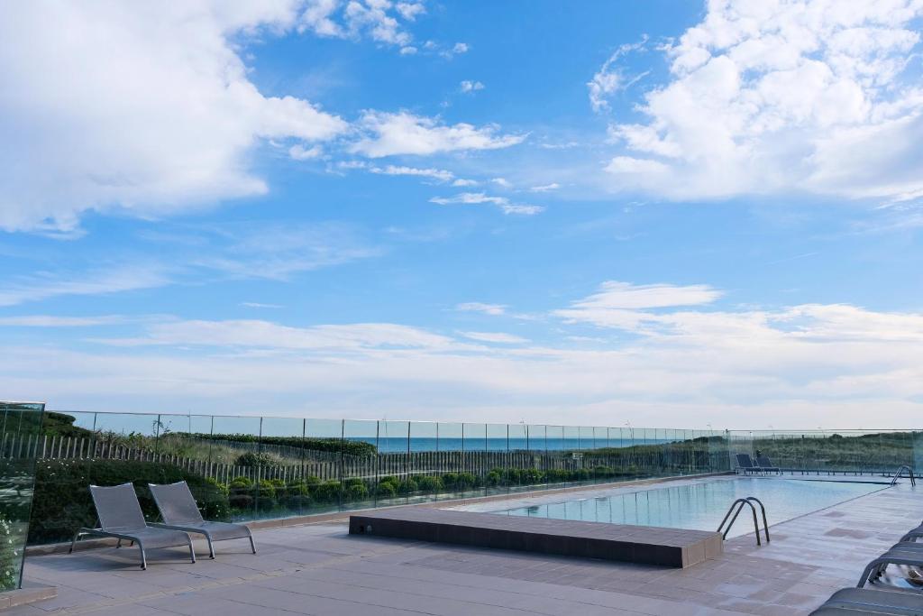 uma piscina com duas cadeiras e o oceano em Thalazur Cabourg - Hôtel & Spa em Cabourg
