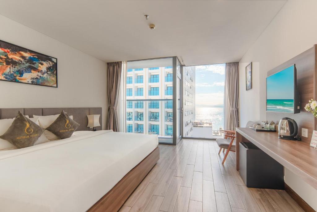 ニャチャンにあるGosia Hotelのベッド、デスク、大きな窓が備わるホテルルームです。