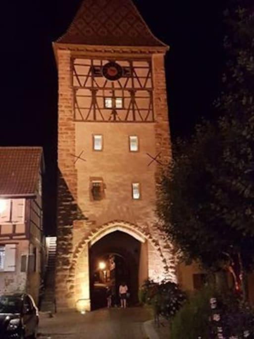 un grand bâtiment en briques avec une tour d'horloge la nuit dans l'établissement Le clocher aux cigognes au village de Bergheim, à Bergheim