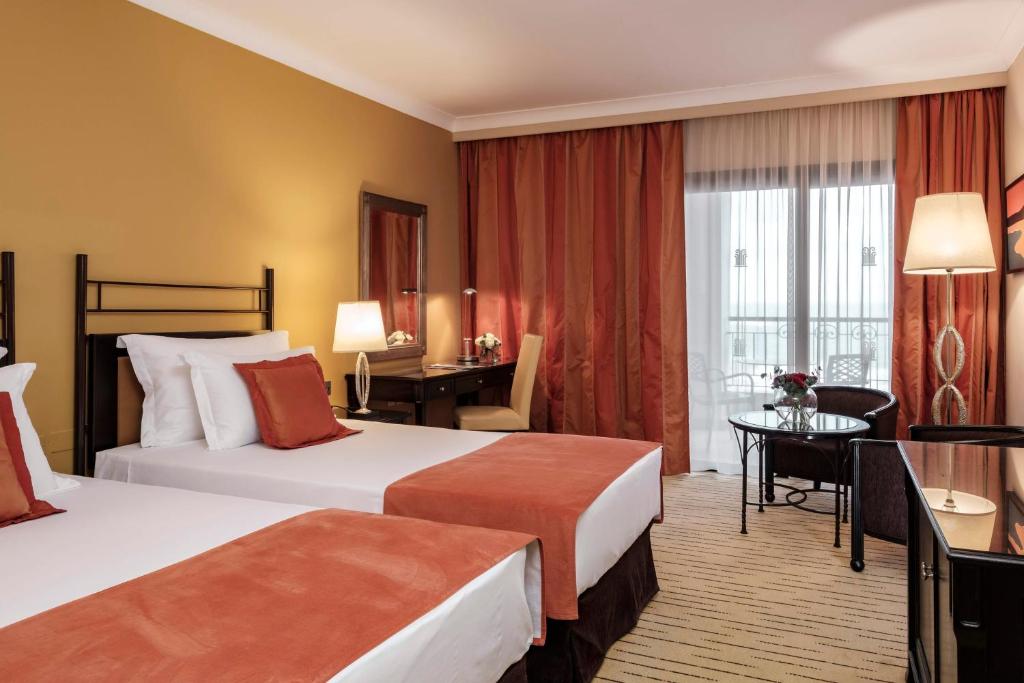 a hotel room with two beds and a desk at Corinthia St George's Bay in St. Julianʼs