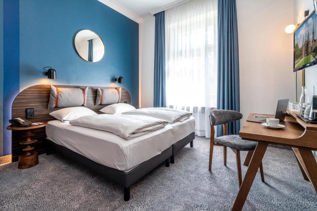 een slaapkamer met een groot bed en een bureau bij Mercure Hotel Luebeck City Center in Lübeck
