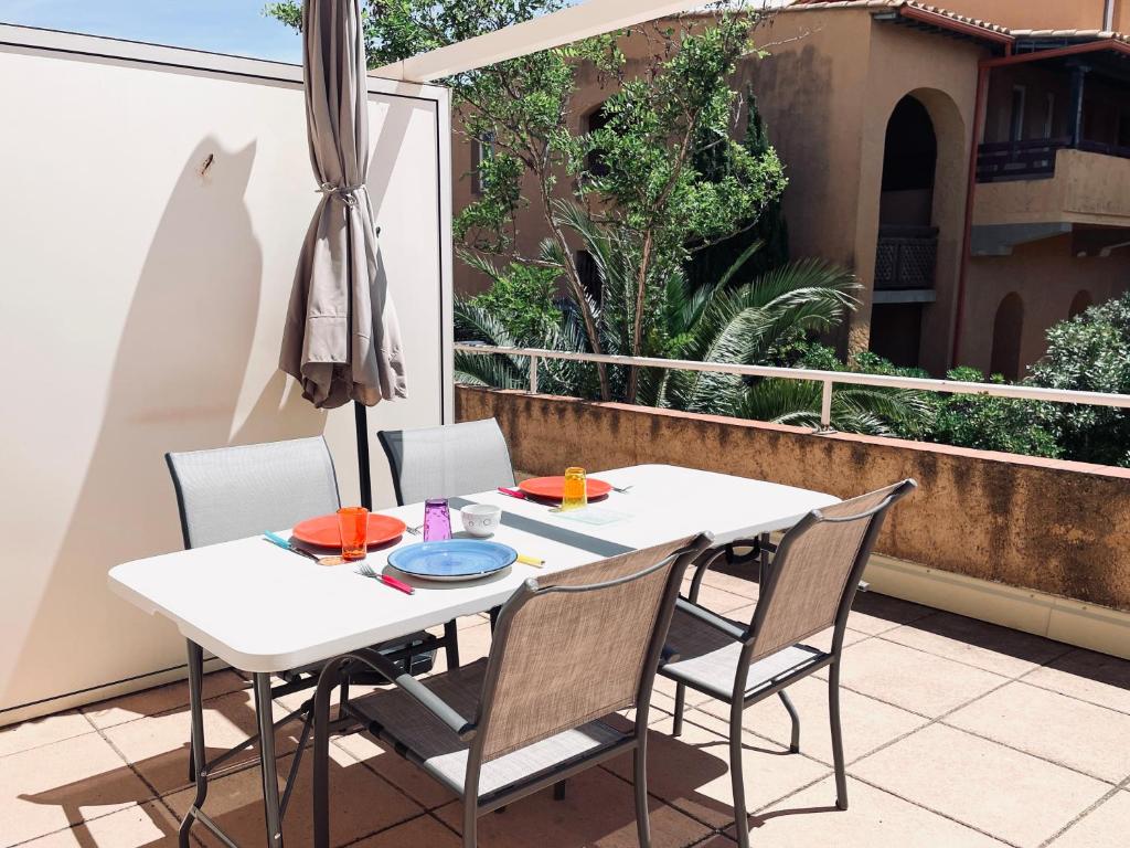 une table et des chaises blanches sur un balcon avec un parasol dans l'établissement Apt 4-6pers-piscine-parc arboré, à Fitou