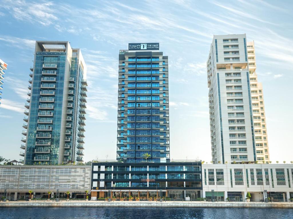 three tall buildings in a city next to the water at The First Collection Waterfront in Dubai