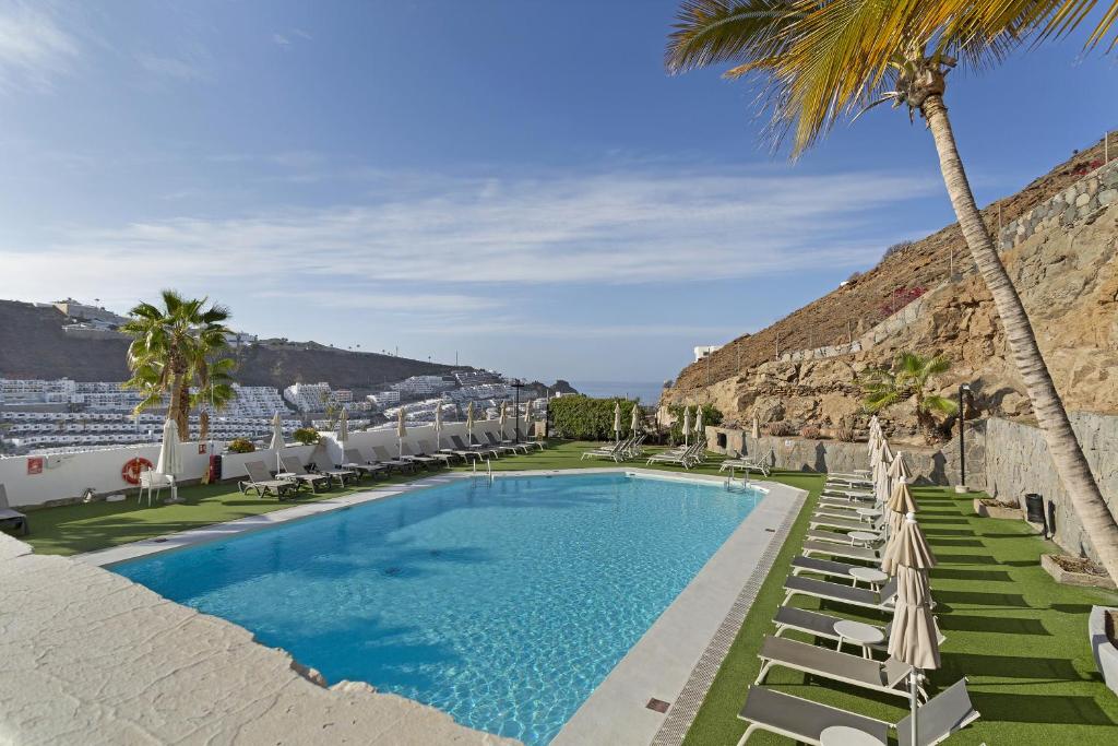 a swimming pool with chaise lounge chairs and palm trees at Enjoy in Puerto Rico de Gran Canaria