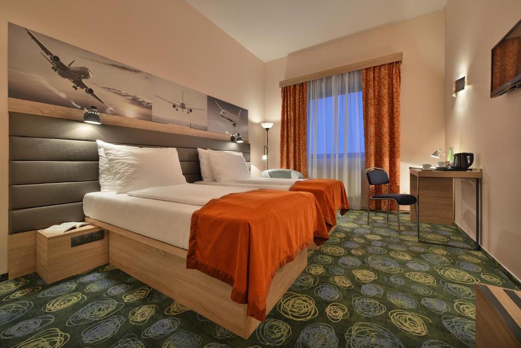 ein Hotelzimmer mit einem großen Bett mit orangefarbener Bettwäsche in der Unterkunft Ramada Airport Hotel Prague in Prag