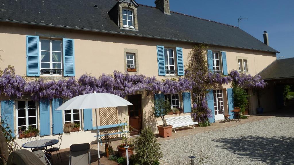 una casa con glicinas púrpuras a un lado en Les Volets Bleus, en Saint-Martin-des-Entrées