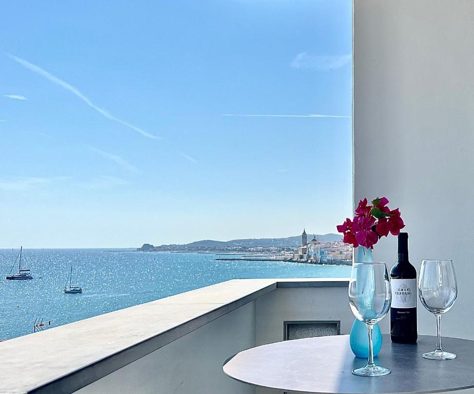 a table with two wine glasses and a vase with flowers at Vistas Del Mar by Hello Homes Sitges in Sitges