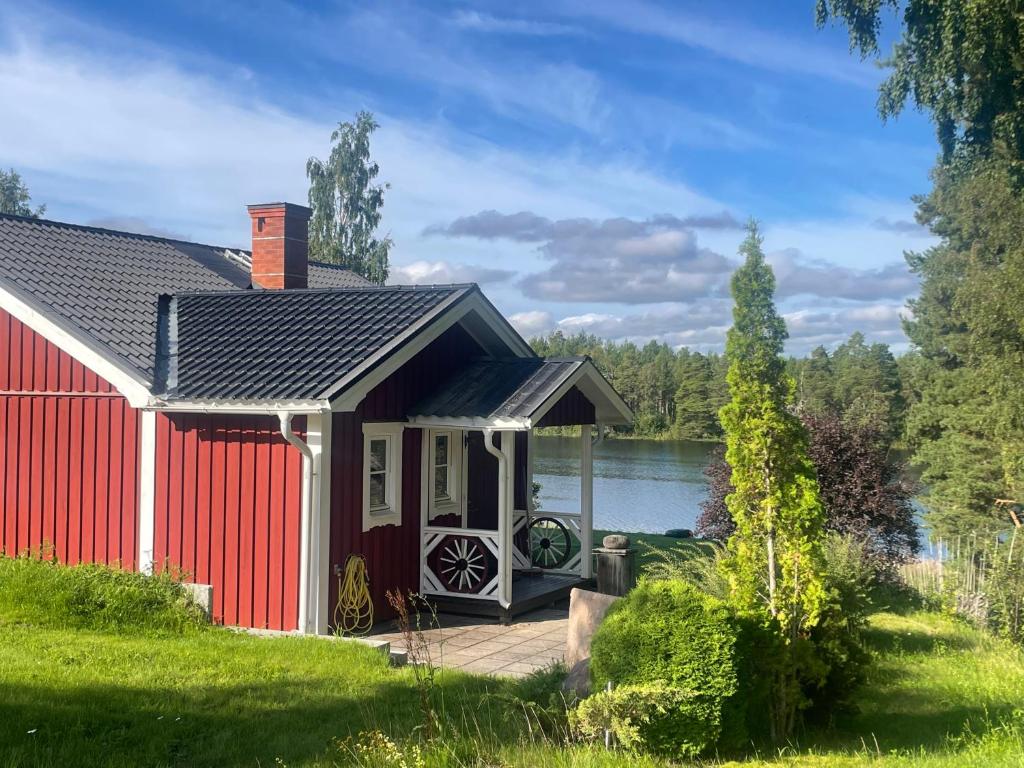 a red house with a deck next to a lake at The Pintorp cabin by the lake in Mora