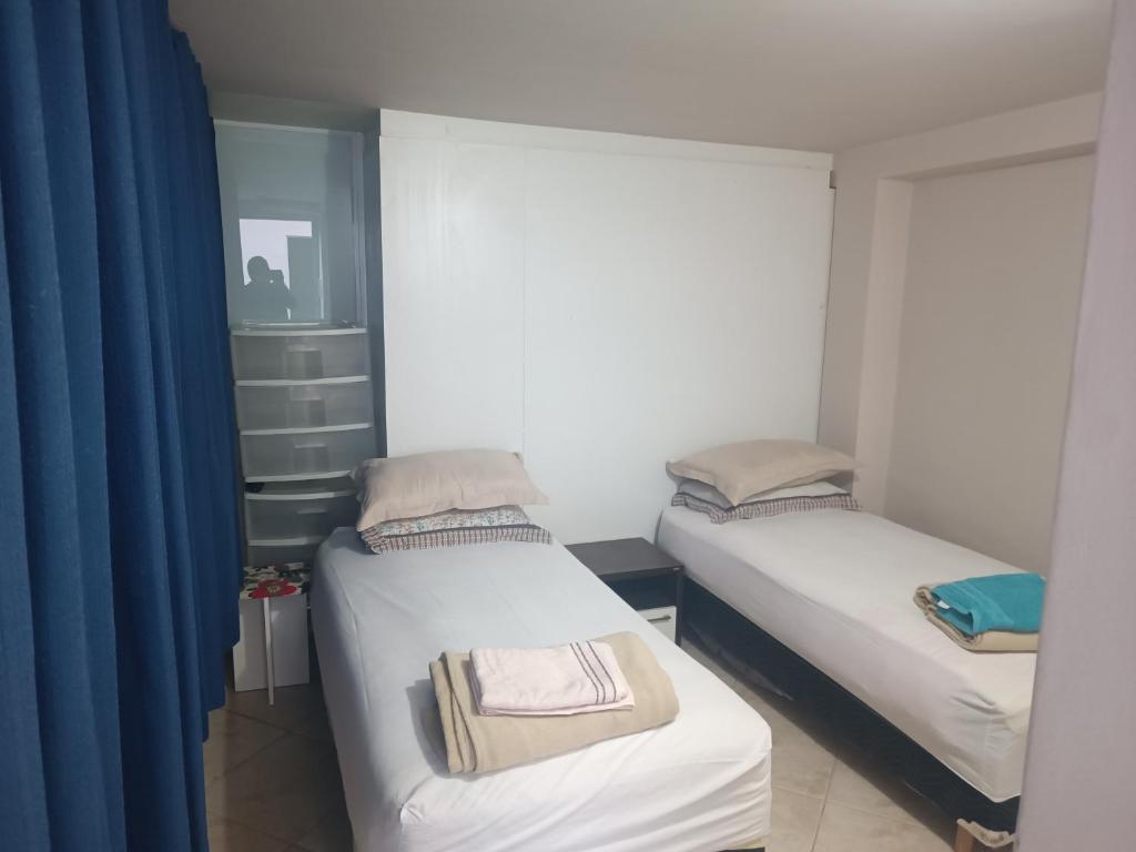 Duas camas num pequeno quarto com cortinas azuis em Assel Pousada Botanico em Curitiba