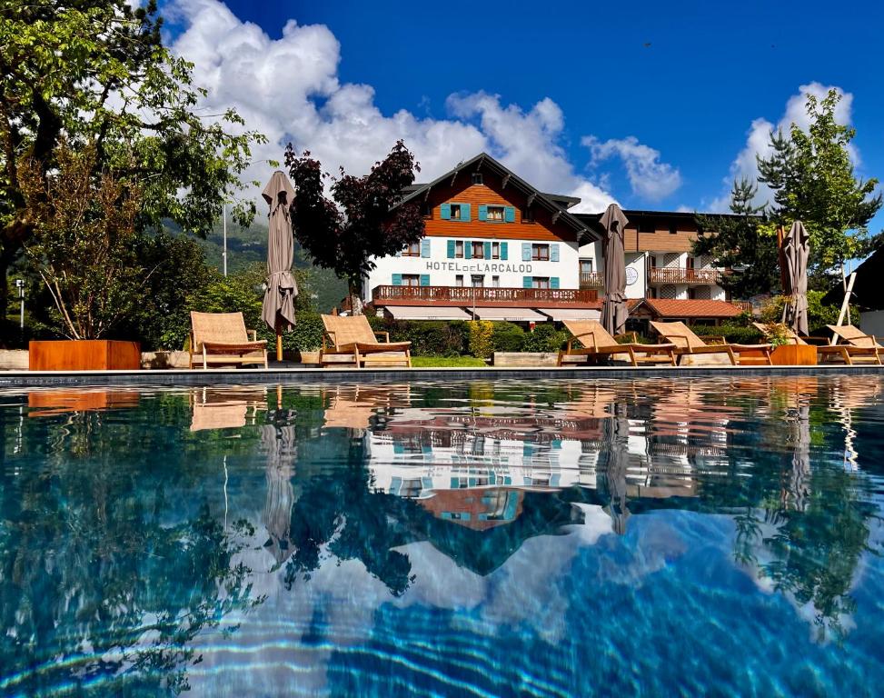 a swimming pool with chairs and a house in the background at L'Arcalod Lac d'Annecy - Hôtel Restaurant & Spa in Doussard