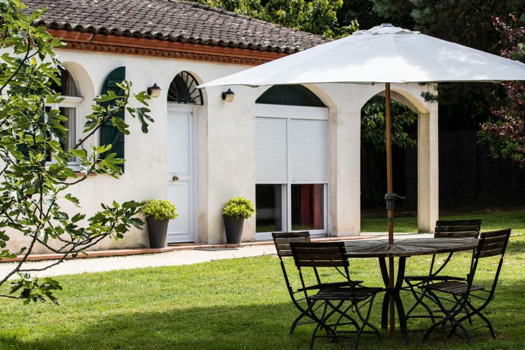 einen Tisch und Stühle mit einem Regenschirm vor einem Haus in der Unterkunft Le Domaine du Vert bois in Pibrac