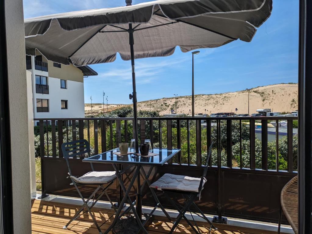 une table et des chaises sur un balcon avec un parasol dans l'établissement Le DÉLICE DES DUNES, à Seignosse