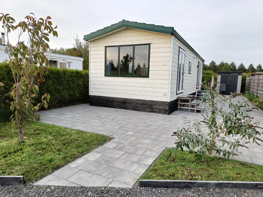 een klein wit huis met een patio in een tuin bij Cozy chalet near Amsterdam at Camping Venhop in Berkhout