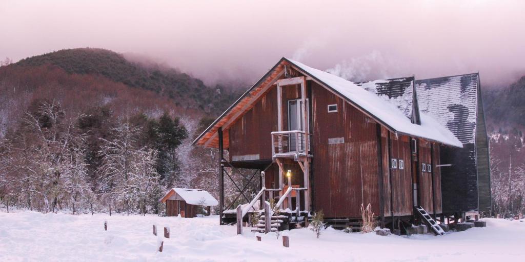 a wooden cabin in the snow with a mountain at Hostal Dos Volcanes in Malalcahuello