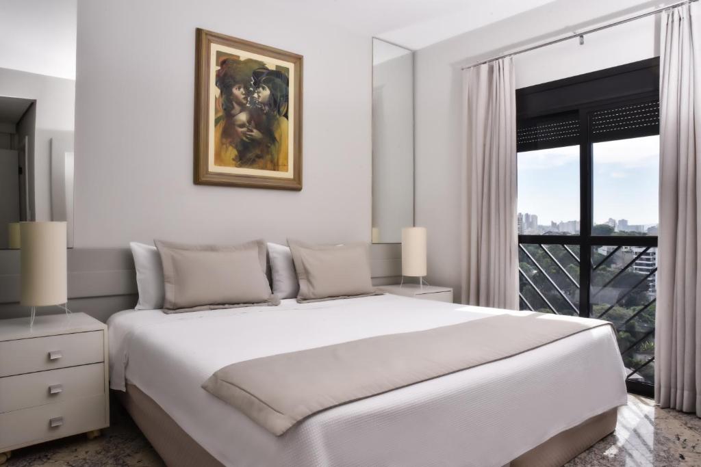 a white bedroom with a large bed and a window at Plaza Inn Small Town Flat in Sao Paulo