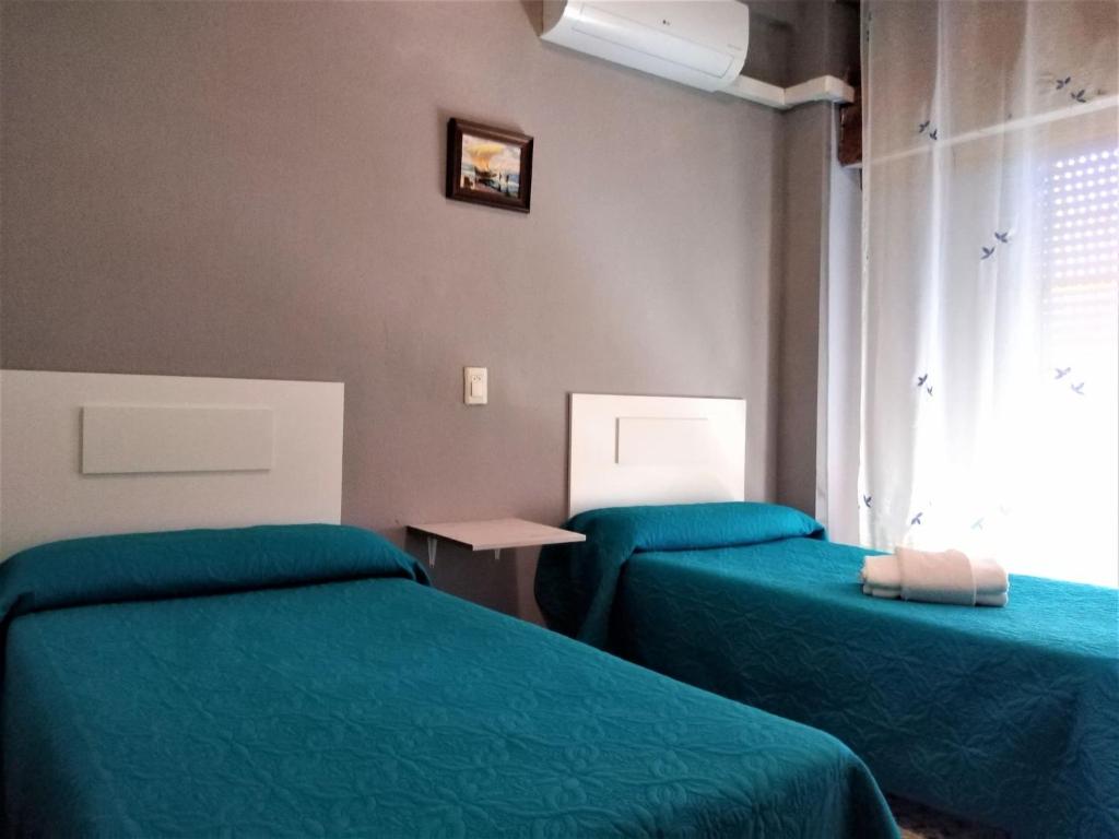 クリェラにあるHabitaciones de Hostal a Primera linea de playa en Culleraの緑のベッド2台と窓が備わる客室です。