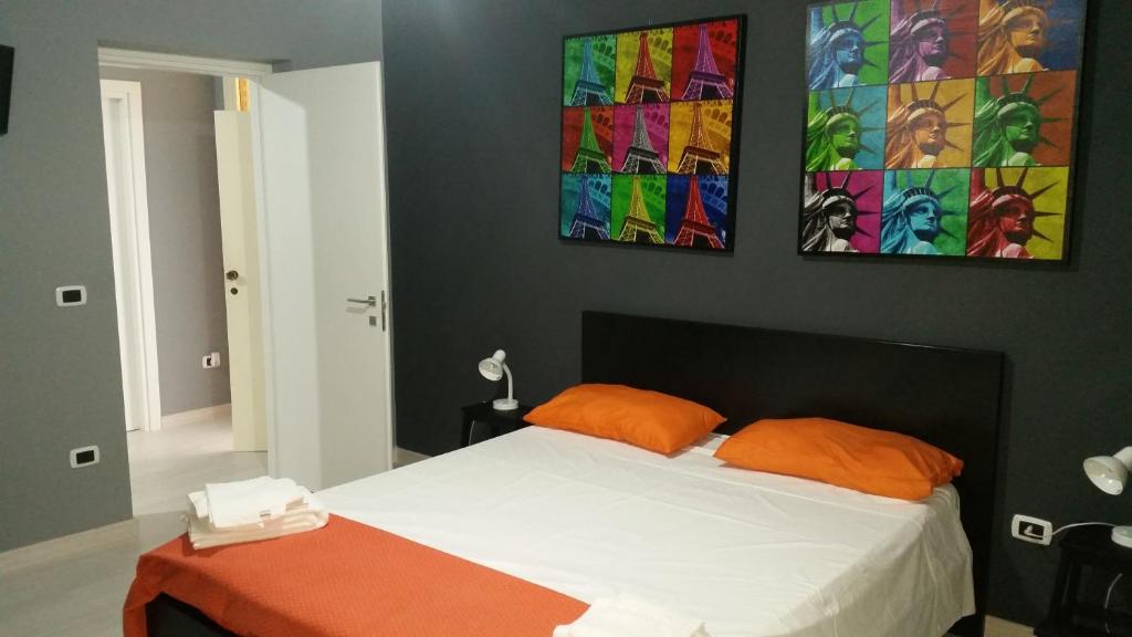 ein Schlafzimmer mit einem Bett mit orangefarbenen Kissen und Gemälden an der Wand in der Unterkunft B&B Colors in Sellia Marina
