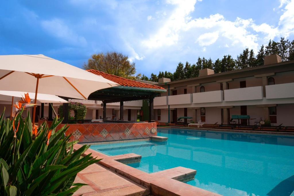 a swimming pool with an umbrella next to a hotel at Villas Arqueologicas Cholula in Cholula