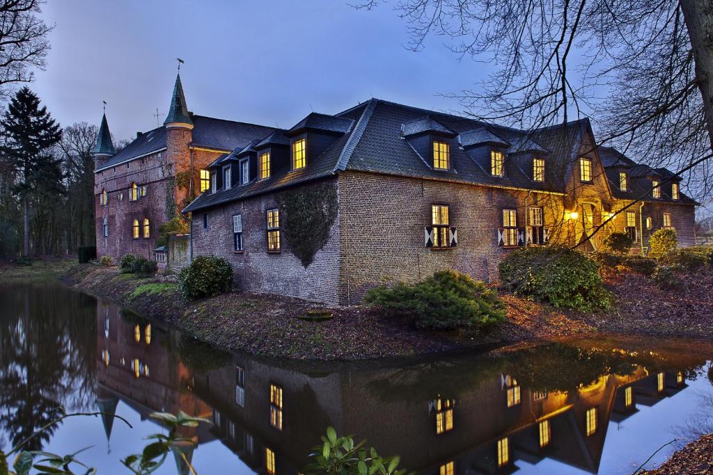 ein großes Haus mit Spiegelung im Wasser in der Unterkunft Hotel Schloss Walbeck in Geldern