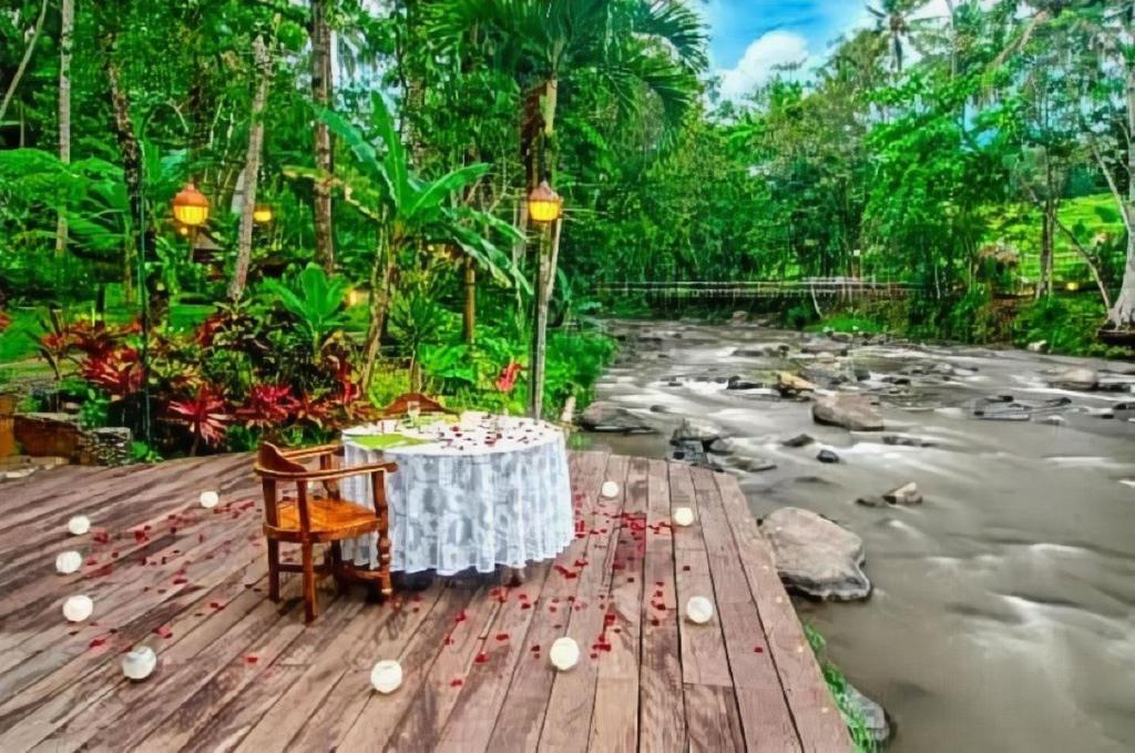 einen Tisch und einen Stuhl auf einer Holzterrasse neben einem Fluss in der Unterkunft Permata Ayung Private Estate in Ubud