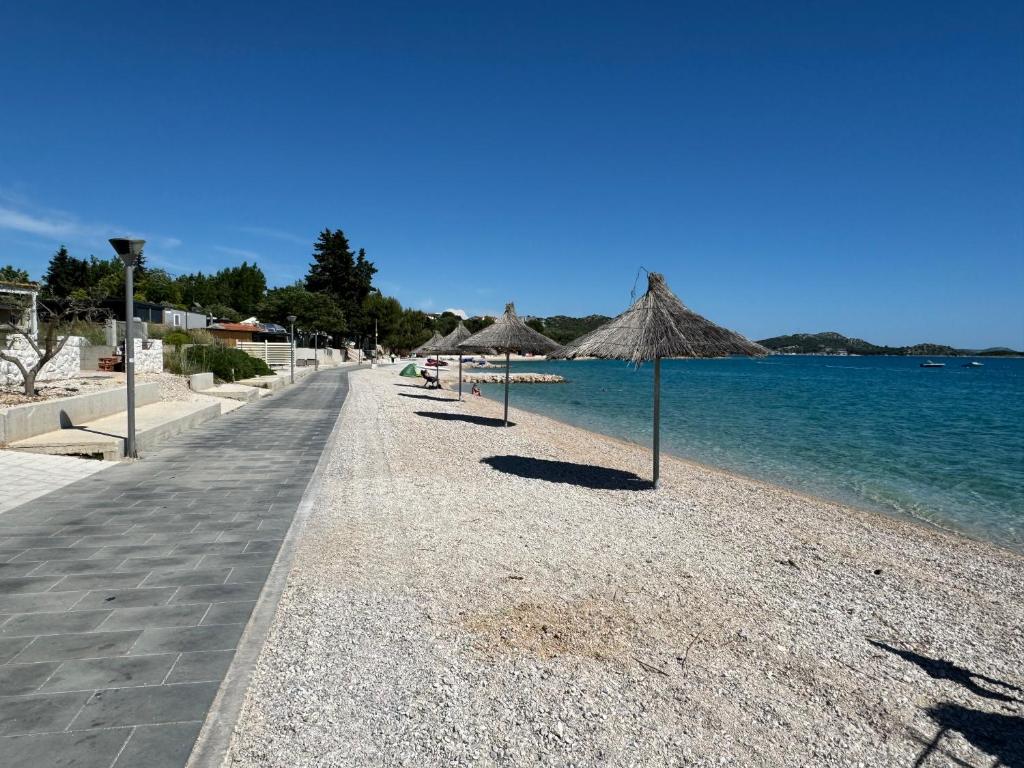 a beach with straw umbrellas and the water at Beach house Chris in Pakoštane