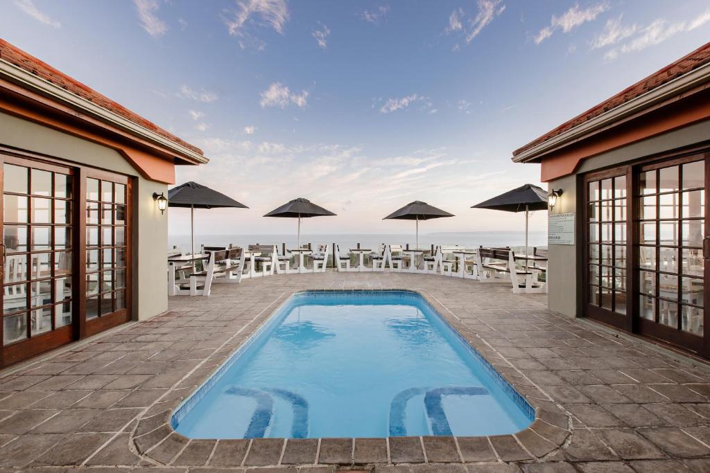 a swimming pool with chairs and umbrellas on a patio at Garden Route Ilita Lodge in Great Brak River