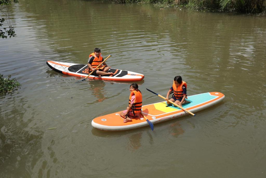 three people in orange shirts are on kayaks in the water at Cần Thơ Farmstay in Can Tho