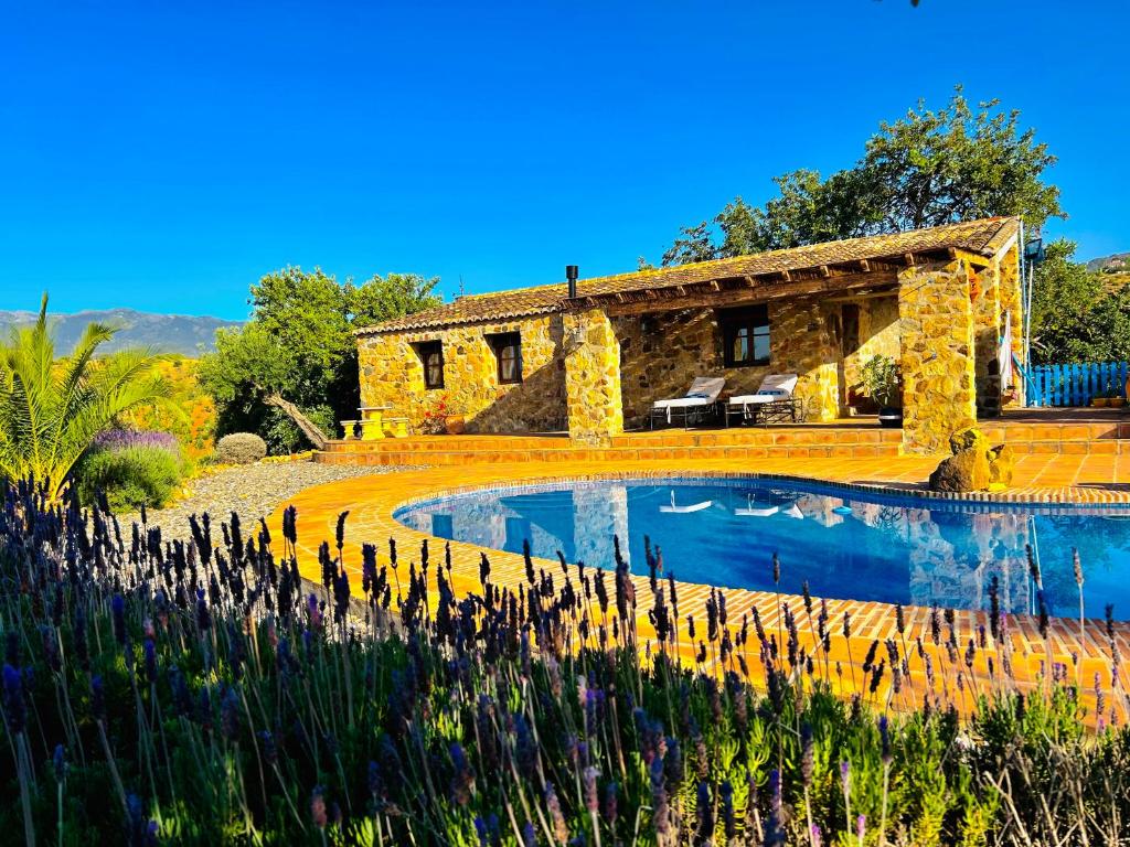 een stenen huis met een vijver ervoor bij Poolhouse with private pool 360 degrees views over pure nature in Alozaina