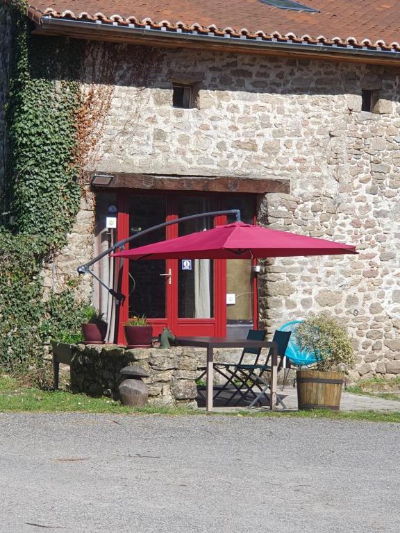 a table with a red umbrella in front of a building at Chambre d’hôtes de Vauguenige in Saint-Pardoux