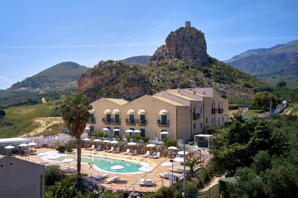 a resort with a pool and mountains in the background at Baglio Dello Zingaro in Scopello