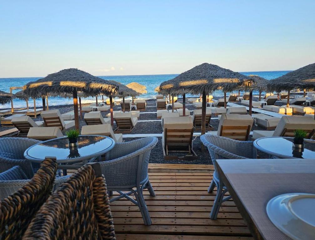 un ristorante sulla spiaggia con tavoli e ombrelloni di paglia di Nostos Beach a Kamari